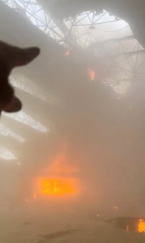 A hand pointing to the ceiling where the roof appears collapsed in a smoke filled room.