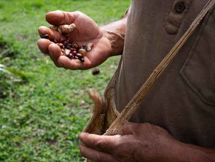 A hand holding seeds next to a woven bag worn across the body