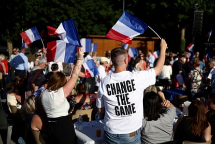 National Rally supporters wave French flags. One male supporter is wearing a T-shirt with the slogan ‘Change the game’