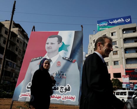 People walk in front of a billboard of the Syrian president, Bashar al-Assad, in Syria.