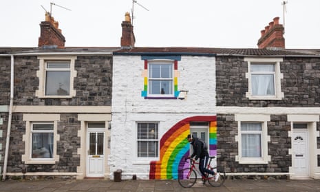 A man in rides his bike past a terrace house in Cardiff painted with a rainbow in support of the NHS.
