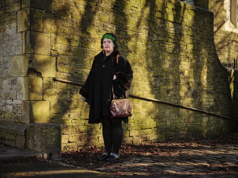 Scout Tzofiya Bolton, a poet and former prisoner, standing against a sun-dappled wall, shadow of trees on it