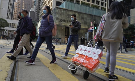 A woman carries a trolley of toilet rolls along a street in hong kong