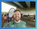 A smiling man in a green running shirt takes a selfie under a bridge at a parkrun event in Japan.