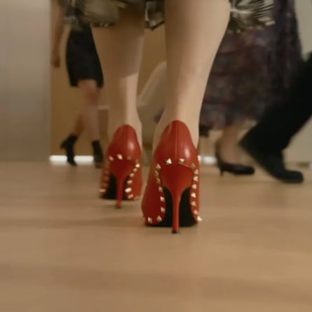 Floor-level view of a woman walking in red high heels with metal studs around the edges