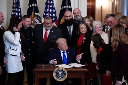 Trump – sat at desk pointing with book open in front of him surrounded by people – participates in the Angel Families remembrance ceremony in the East Room at the White House in Washington.