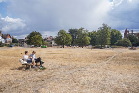 Two men sit on a bench surrounded by scorched dry grass