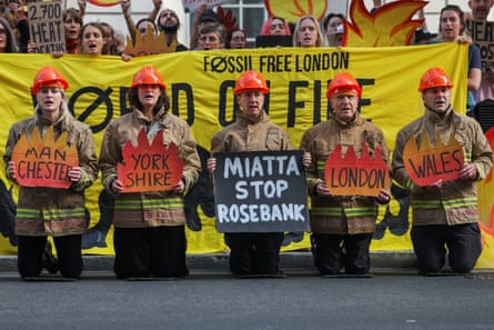People dress in firefighter uniforms and hold signs that say ‘Miatta stop Rosebank’