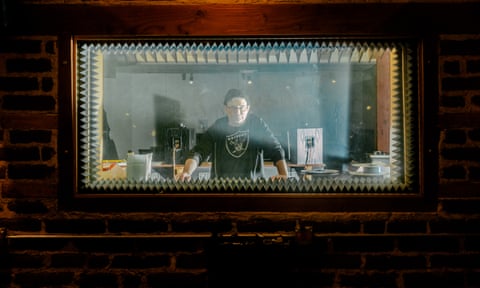 Musician Steve Albini, in a hat, standing in front of record equipment behind a window in his studio