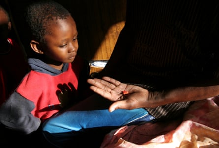 A young black child looks at an adult’s hand holding two tablets