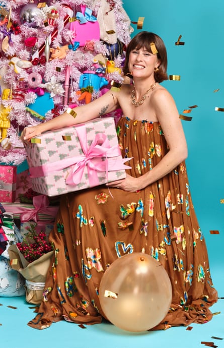 Woman holding Christmas gift in pink wrapping paper, next to a Christmas tree