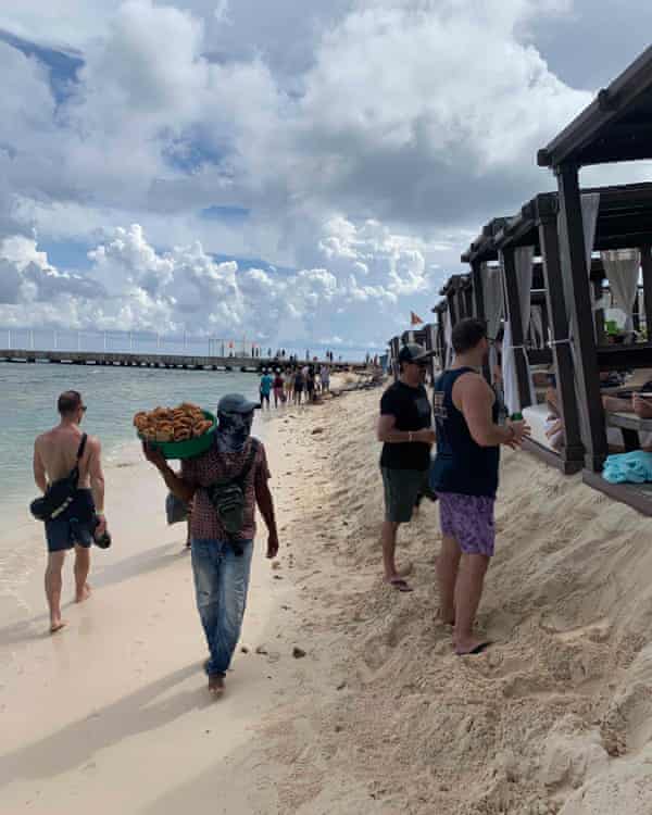 Foreigners and hawkers walk along a thin strip of beach between the sea and tourists’ sun shelters