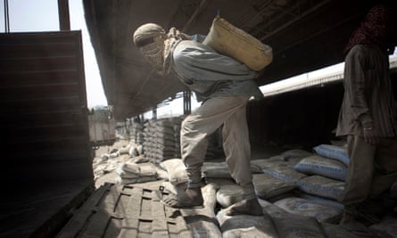Laborers load cement bags manually onto transport carriers at the Shakur Basti station in New Delhi, India.