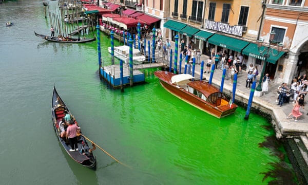 A gondola navigates along Venice’s historical Grand Canal as a patch of phosphorescent green liquid spreads in it.