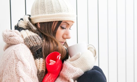 A woman wrapped up at home with a hot water bottle and a hot drink