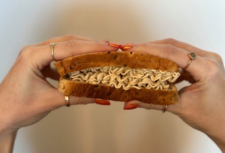 Two hands holding a sandwich filled with uncooked instant noodles.