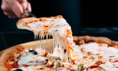 Slice of pizza being lifted from the pie with strands of melted cheese stretching down.