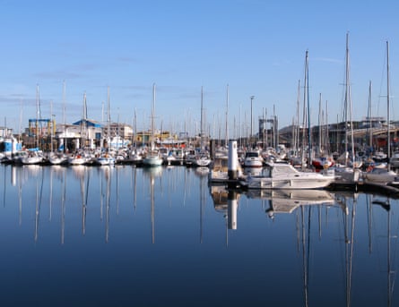 Sailing boats reflected in calm water in a harbour.