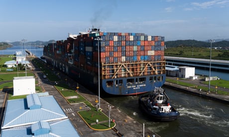 Tall barge, stacked with rows of container units in the Cocolí locks on the Panama canal, followed by a tug boat