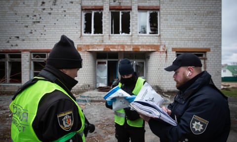 Police officers document the war crimes of the Russian army in the village of Shevchenkove, Ukraine, in front of a building with broken  windows.