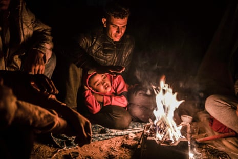 People sit around a makeshift fire to keep warm during cold weather