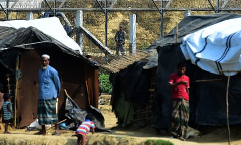 Myanmar security personnel keep watch along the Myanmar-Bangladesh border as Rohingya refugee stand outside their makeshifts shelters in Bangladesh.