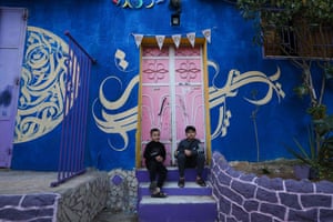 Children sit at the doorstep of a house, painted in vivid colours as part of an initiative by a Palestinian artist, in the Zeitun district of Gaza City