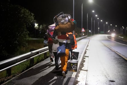 People push a cart carrying their belongings along a dark street