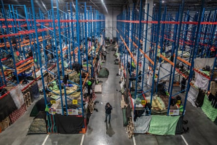 A warehouse with beds set up on shelves where goods would normally be stored