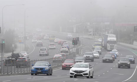 A wide view from the side of a main road of cars and trucks driving in both directions through fog