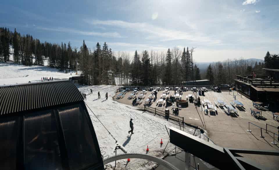 A snowy ski resort has a paved outdoor eating area filled with picnic tables.