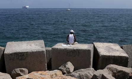 A migrant sits on a concrete block at the Palermo waterfront.