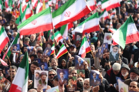 A large mass of people are facing the camera, waving green, white and red Iranian flags and holding photos of Ayatollah Mojtaba Khamenei.