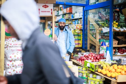 A man stands in the doorway of grocery shop near fruit on display as someone walks past