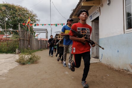 A line of teenagers carrying replica guns and wearing modern clothes run past a building.