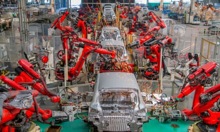 Red robot arms to left and right of a car assembly line