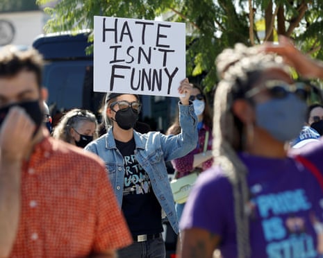 A masked woman in a denim jacket holds a sign above her head reading 'Hate Isn't Funny' at an October rally supporting Netflix employees protesting Dave Chappelle's special