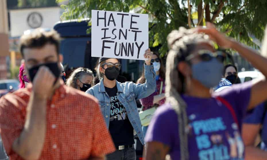 A masked woman in a denim jacket holds a sign above her head reading 'Hate Isn't Funny' at an October rally supporting Netflix employees protesting Dave Chappelle's special