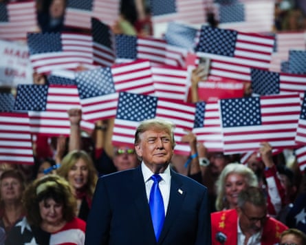 Trump standing in front of a large crowd holding individual US flag cutouts.