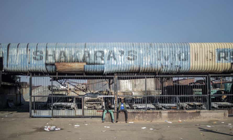 Two men sit in front of a burned down car showroom in Jeppestown district, Johannesburg, on July 11, 2021, damaged on the night of violence following protests over jailing of former president Jacob Zuma.
