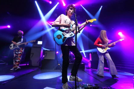 A picture of a rock band with a pink and blue light show behind them