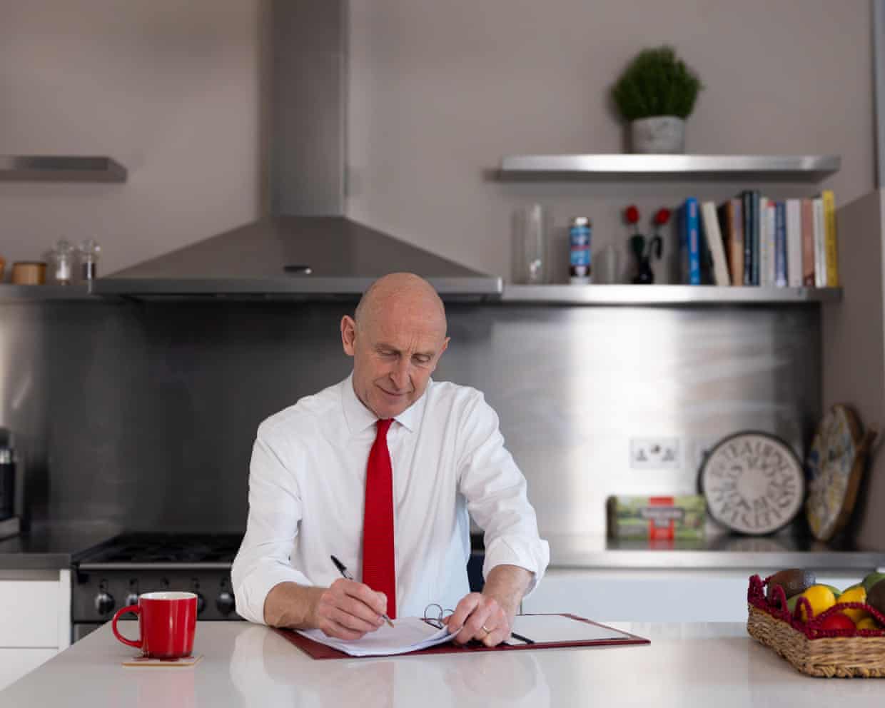 John Healey, jacket off, at kitchen table working on papers
