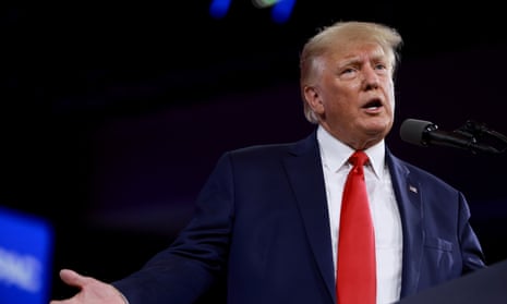 Trump, wearing a red tie, speaks into a mic.