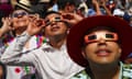 people wearing paper eclipse glasses look up at the eclipse