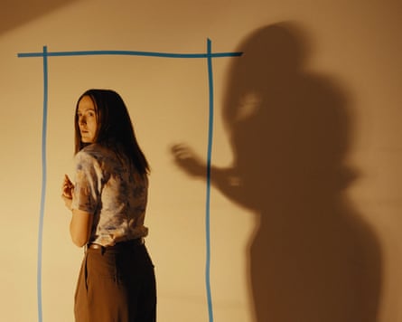 woman looks behind her, with her shadow cast on a yellow wall