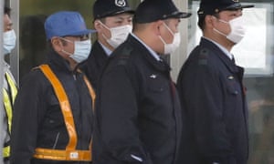 Former Nissan chair Carlos Ghosn, in blue cap, walks out with security guards from a detention centre in Tokyo.