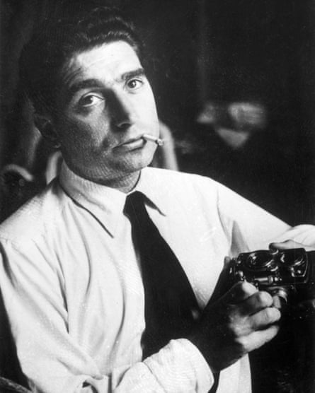 Robert Capa with a smouldering cigarette between his lips holds a camera