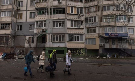 People with their luggage walk past a damaged residential building in Kherson.