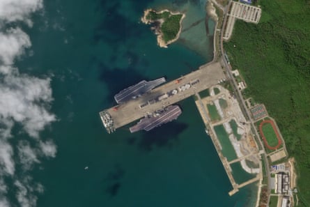 Satellite image of two aircraft carriers in water next to jetty
