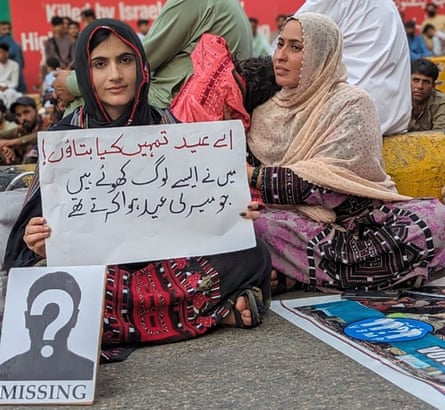 Sammi Deen Baloch, left, and Seema Baloch, sit on the ground holding placards at a protest.